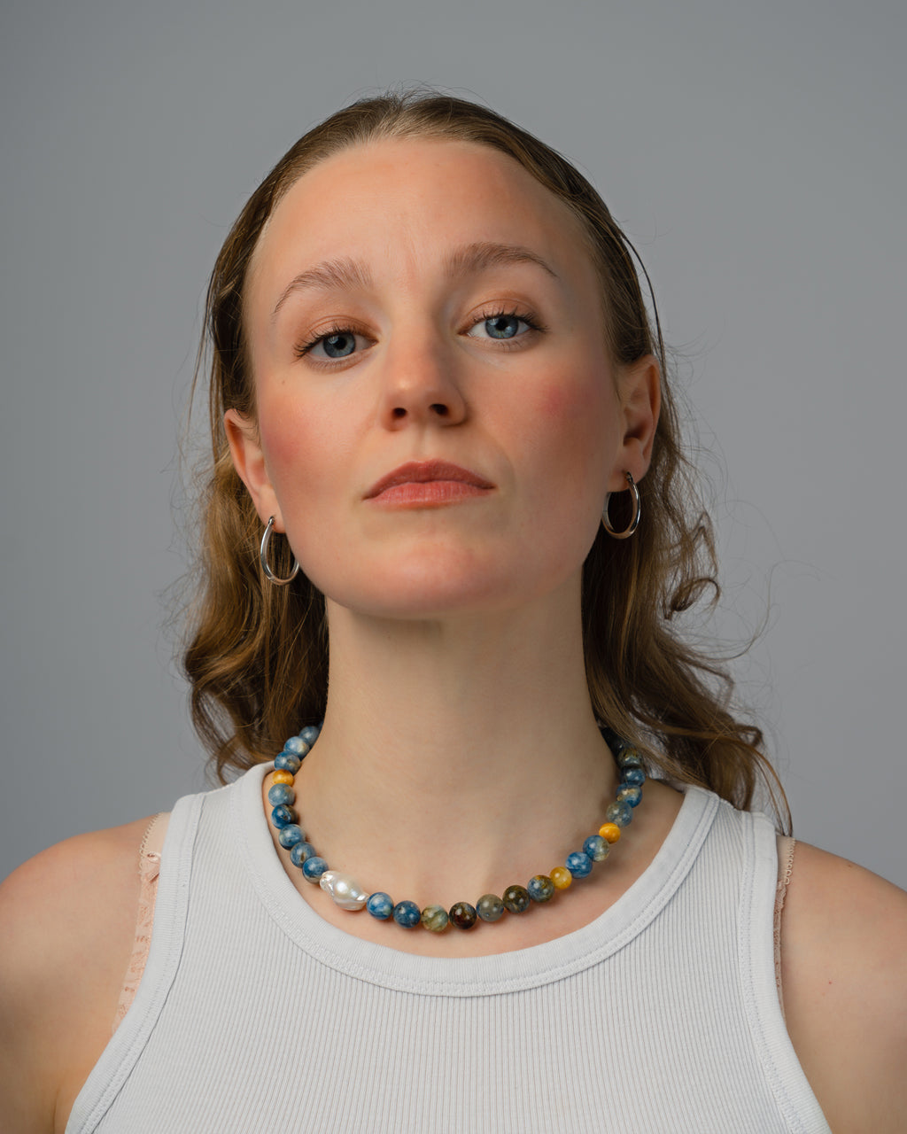 Woman wearing a colorful beaded necklace against a gray background