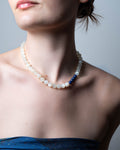 Pearl necklace with a blue bead worn by a person against a neutral background