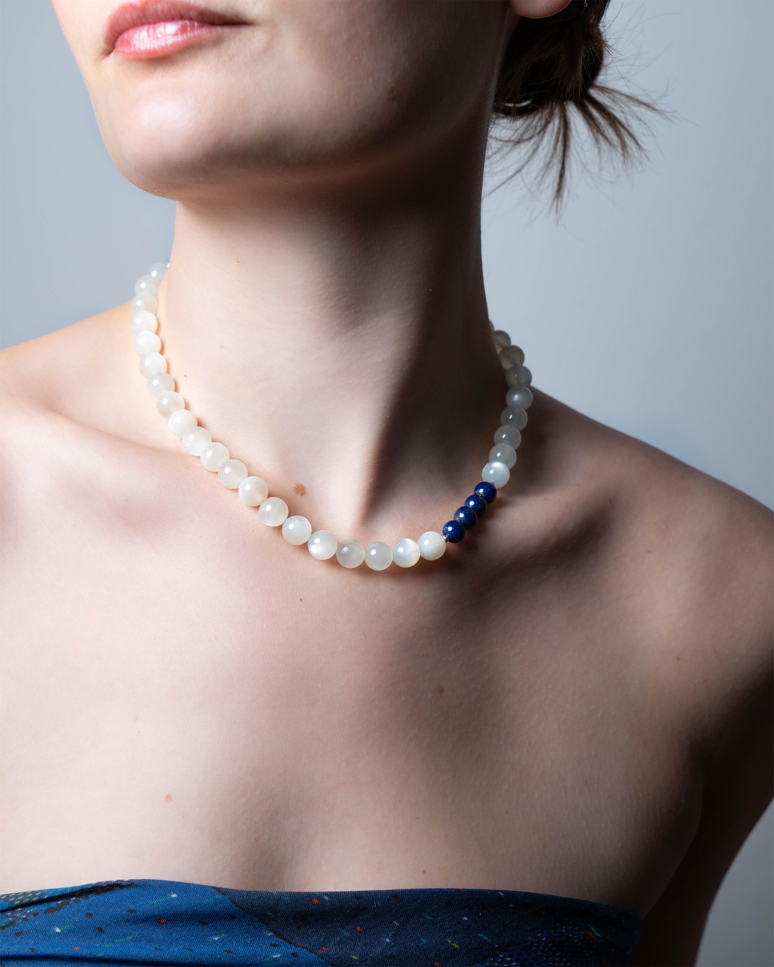 Pearl necklace with a blue bead worn by a person against a neutral background